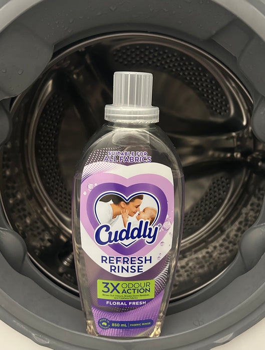 A bottle of Cuddly Refresh Rinse placed inside the drum of a washing machine.